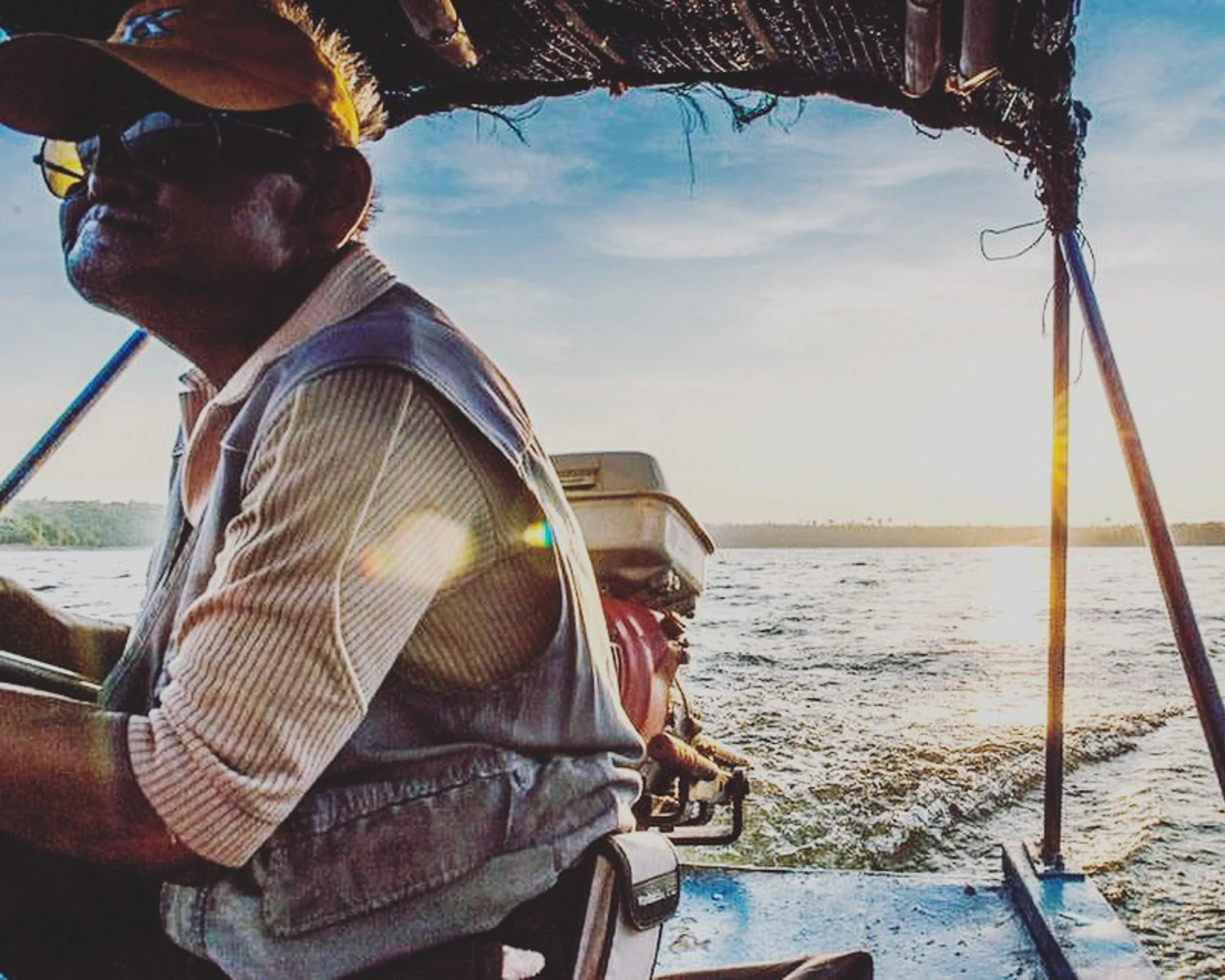 Boat skipper in silhouette steering along a sunlit river at dusk