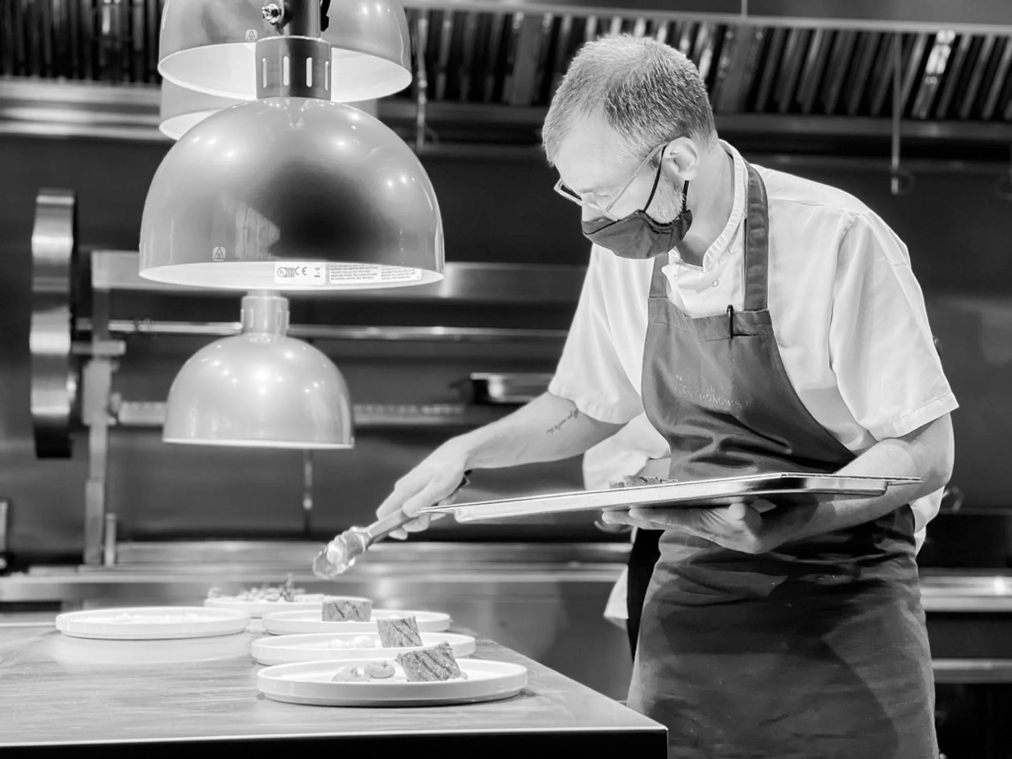 Black and white shot of a chef plating dishes in a professional kitchen, brand storytelling photography by Hector's Eye for Wyatt & Jones