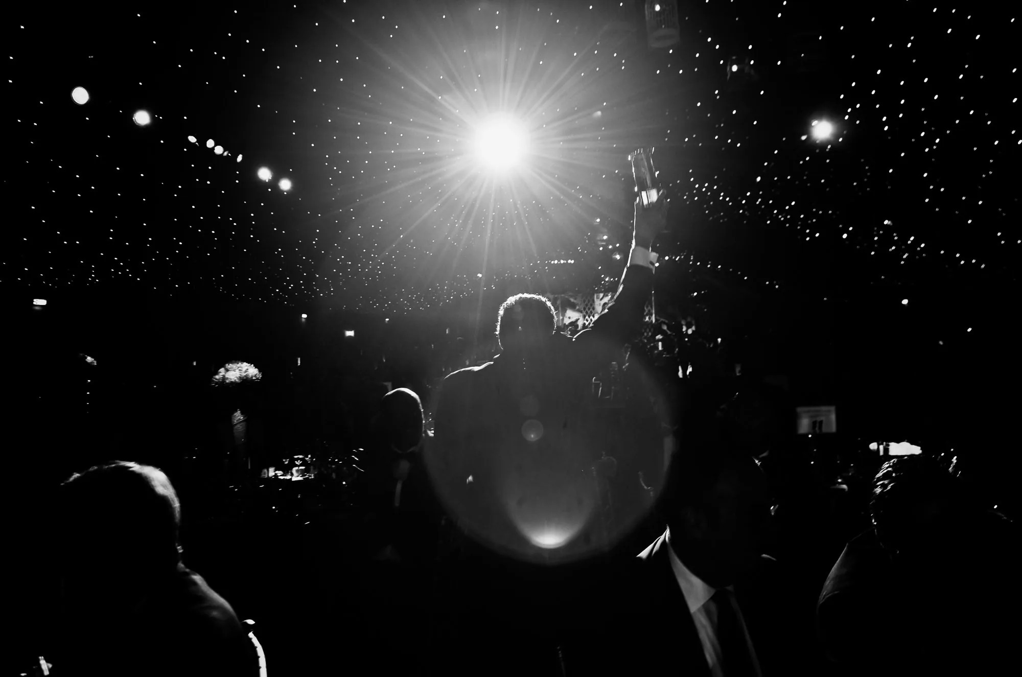 Silhouetted guest raising a trophy beneath a starburst of stage lighting and bokeh, corporate awards dinner photography by Hector's Eye