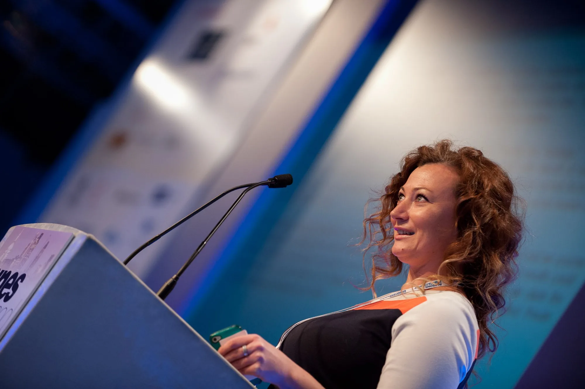 Female speaker smiling from behind a podium at a corporate conference, event photography by Hector's Eye