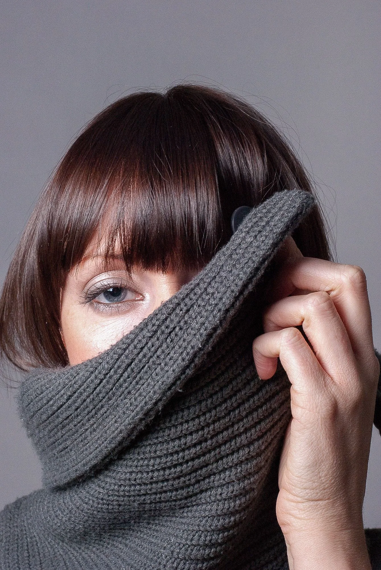 Editorial portrait of a woman with a grey knitted scarf pulled up over her face, studio portrait photography by Hector's Eye