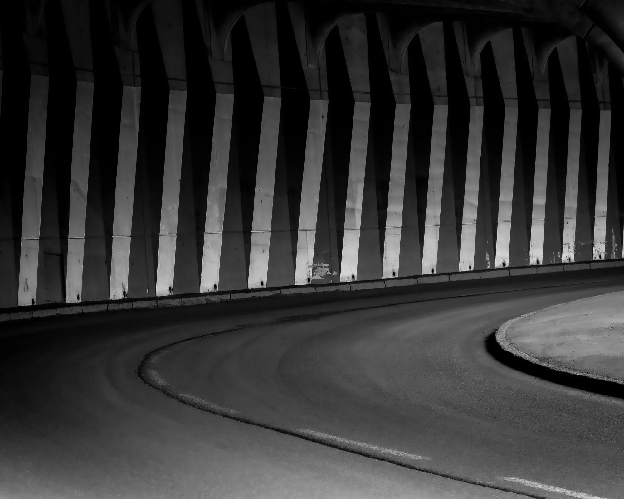 Black and white symmetrical view of a curving urban underpass, street photography by Hector's Eye